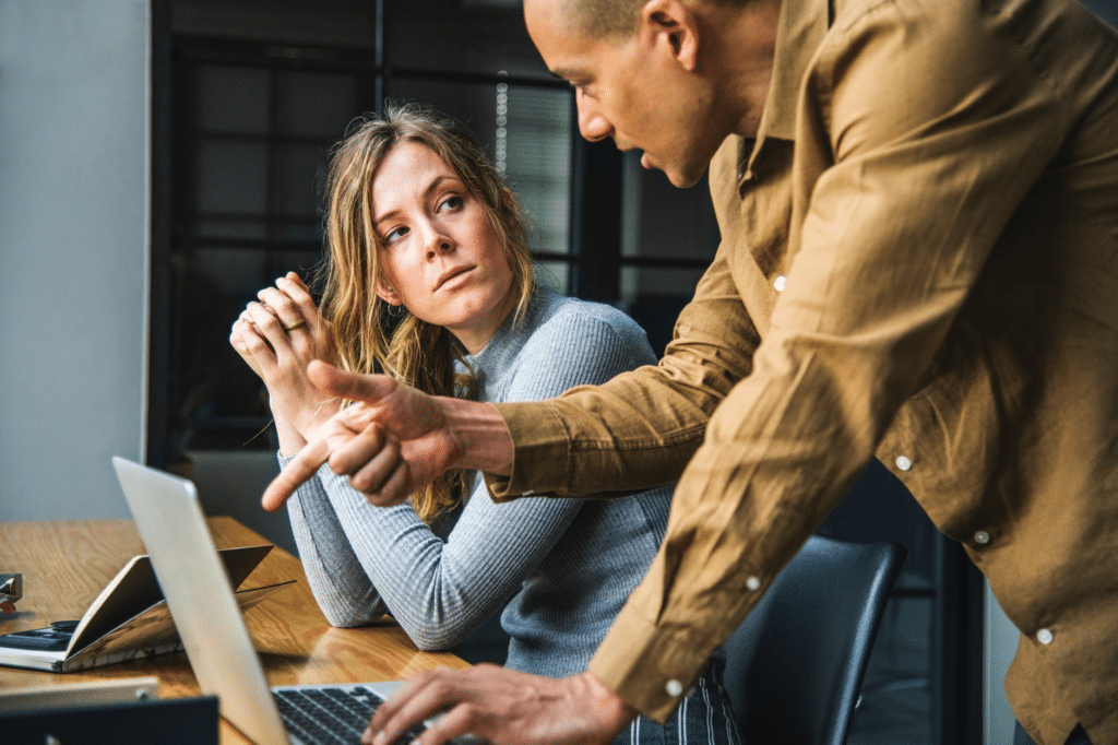 Employee pointing at laptop while talking to coworker